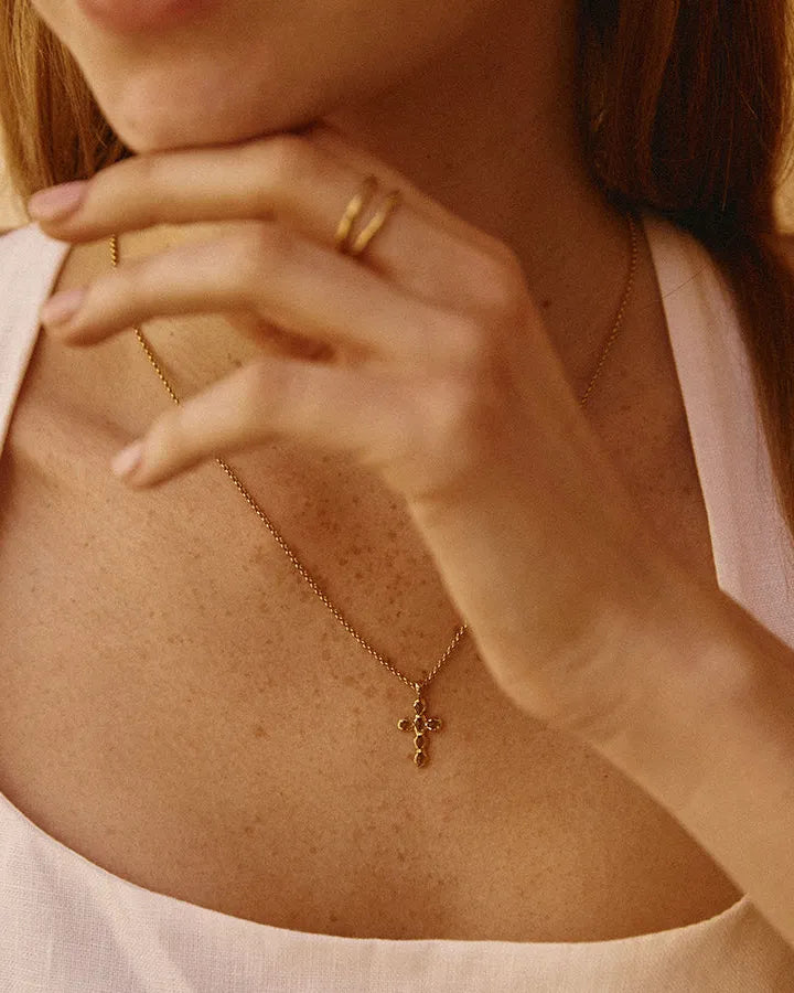 Gold Nexa Necklace with a small cross pendant featuring oval green stones, worn on a woman's chest.