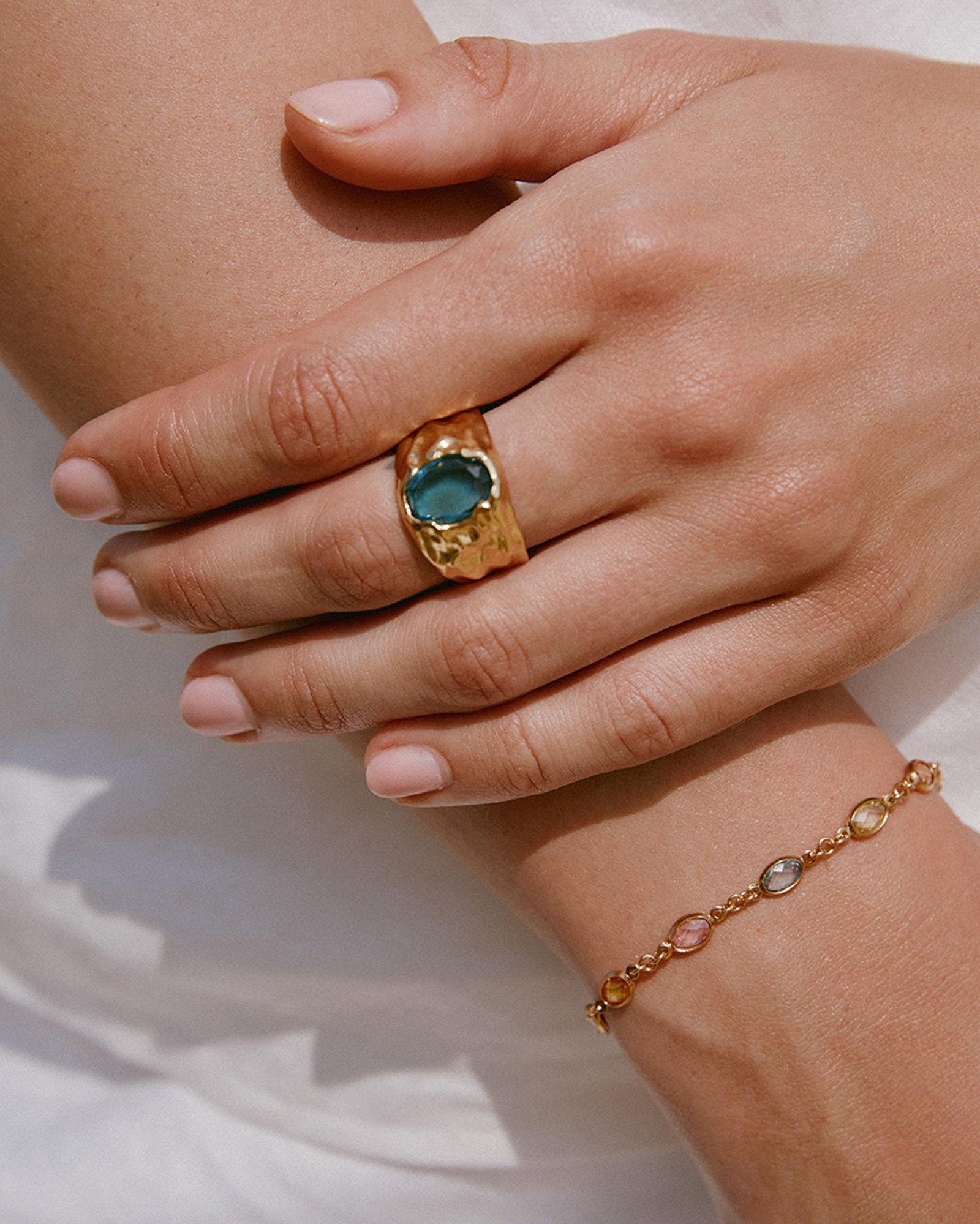 Fruitera Primavera bracelet with multicolored stones on a fine gold chain, worn with a gold ring.