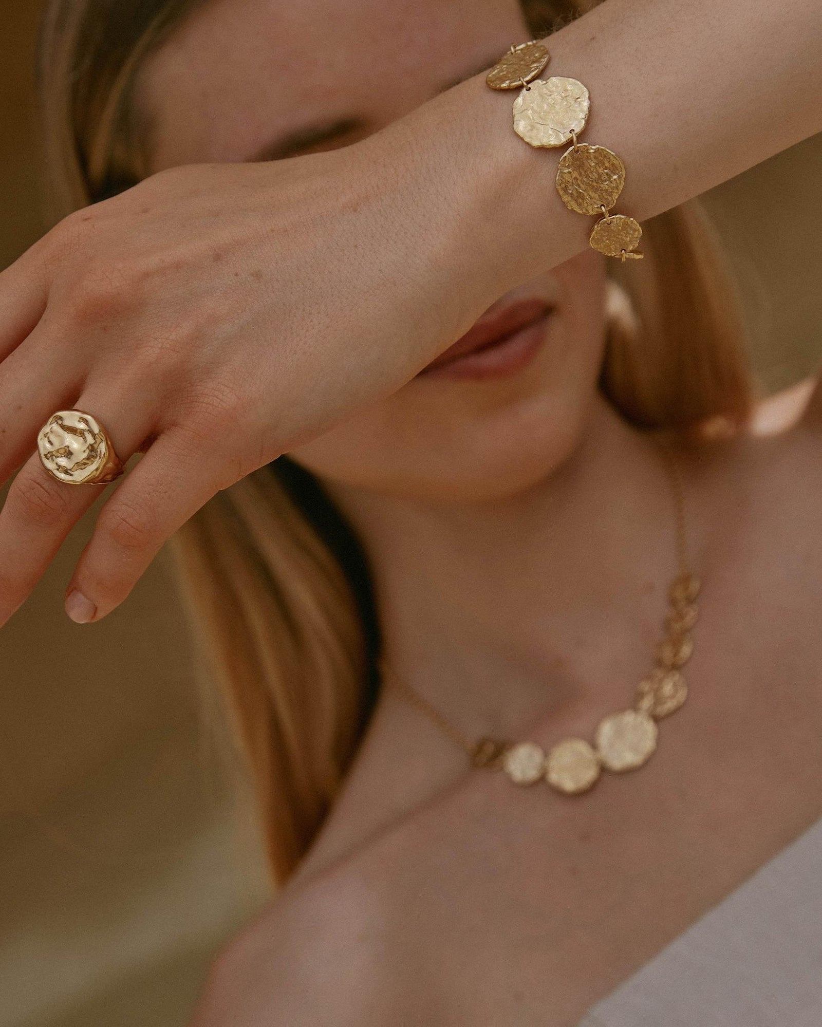 Golden Cassia bracelet with 9 hammered discs on a woman's wrist, matching necklace and ring.