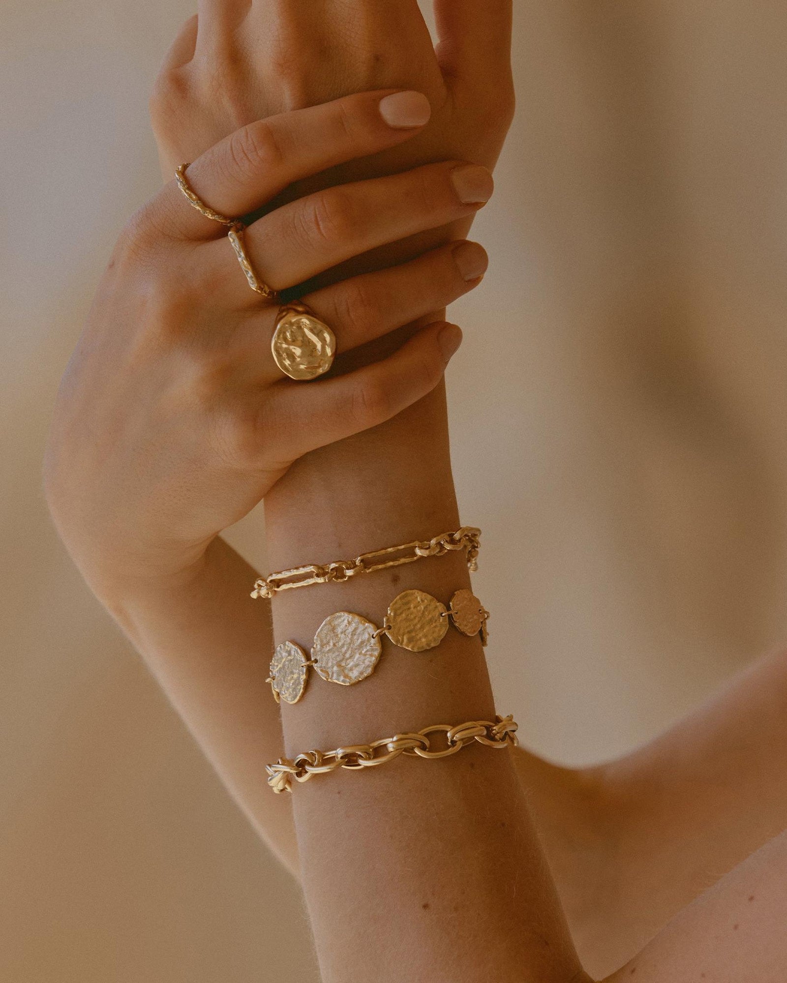 Golden Cassia bracelet with 9 hammered discs on a woman's arm, styled with other gold jewelry.
