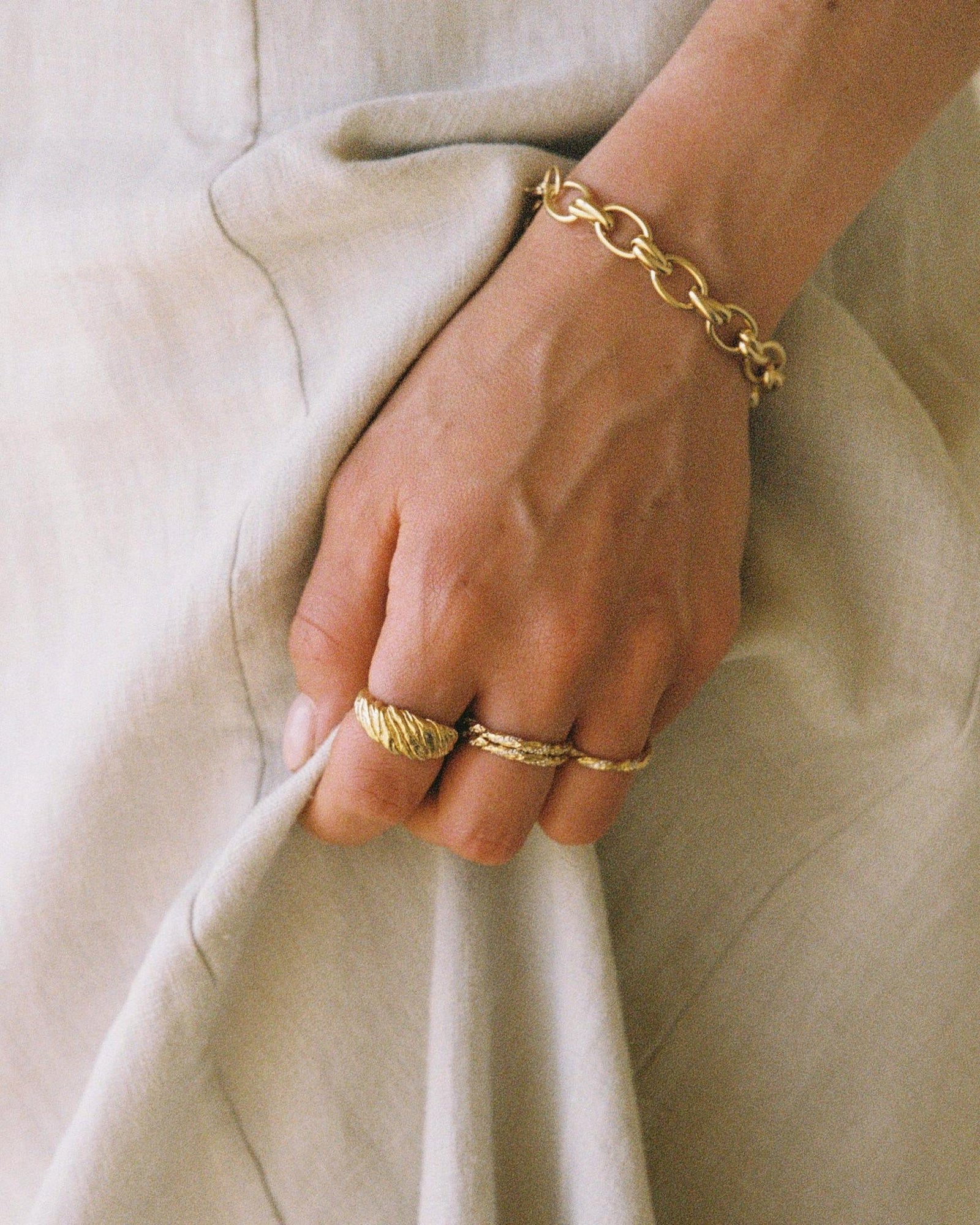 Gold Alessia rolo chain bracelet with interlocking links on a wrist, alongside three gold rings.