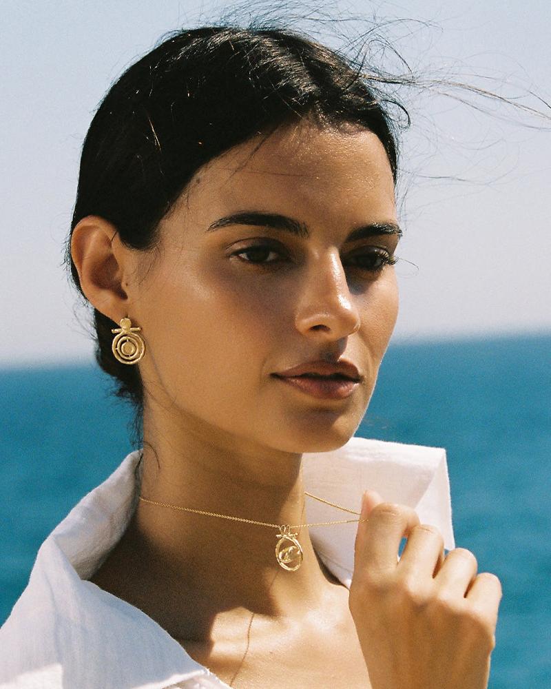 Woman wearing a gold Gali necklace with a spinning sun pendant and matching astrolabe earrings.
