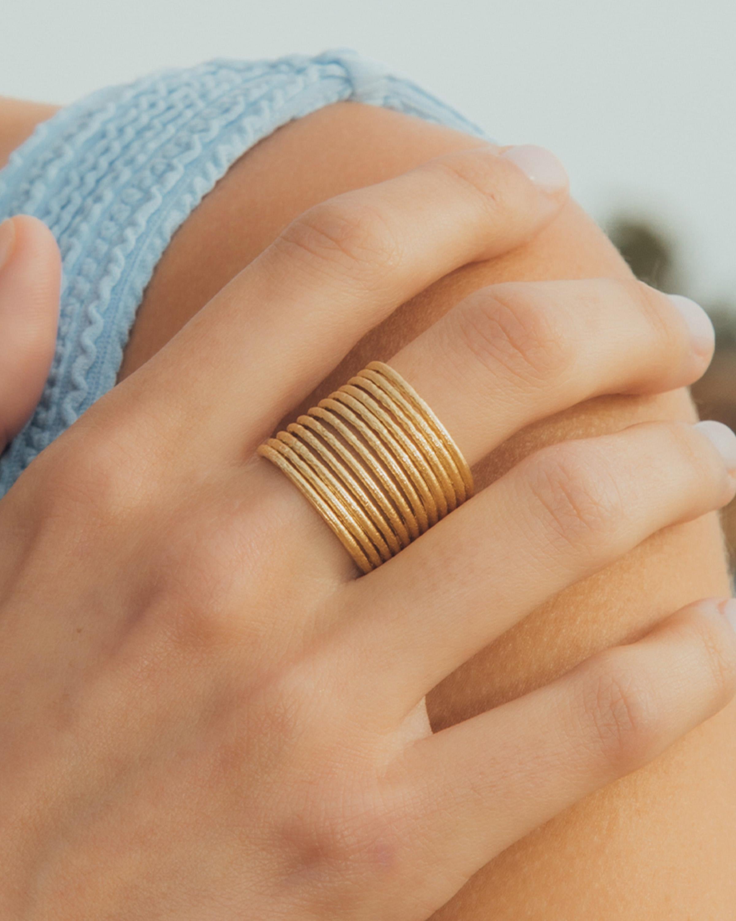 Anello regolabile Etérea dorato con 12 delicate fasce sovrapposte, indossato al dito.