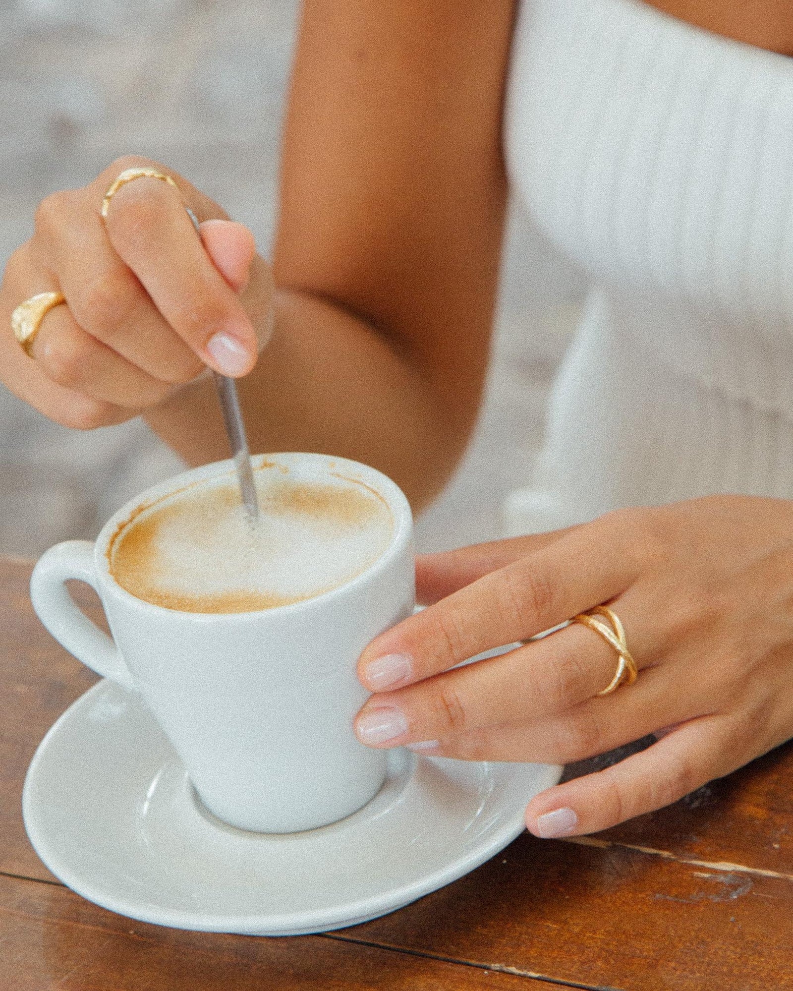 Woman's hands stirring coffee, wearing a gold Alta ring with an elegant criss-cross design.