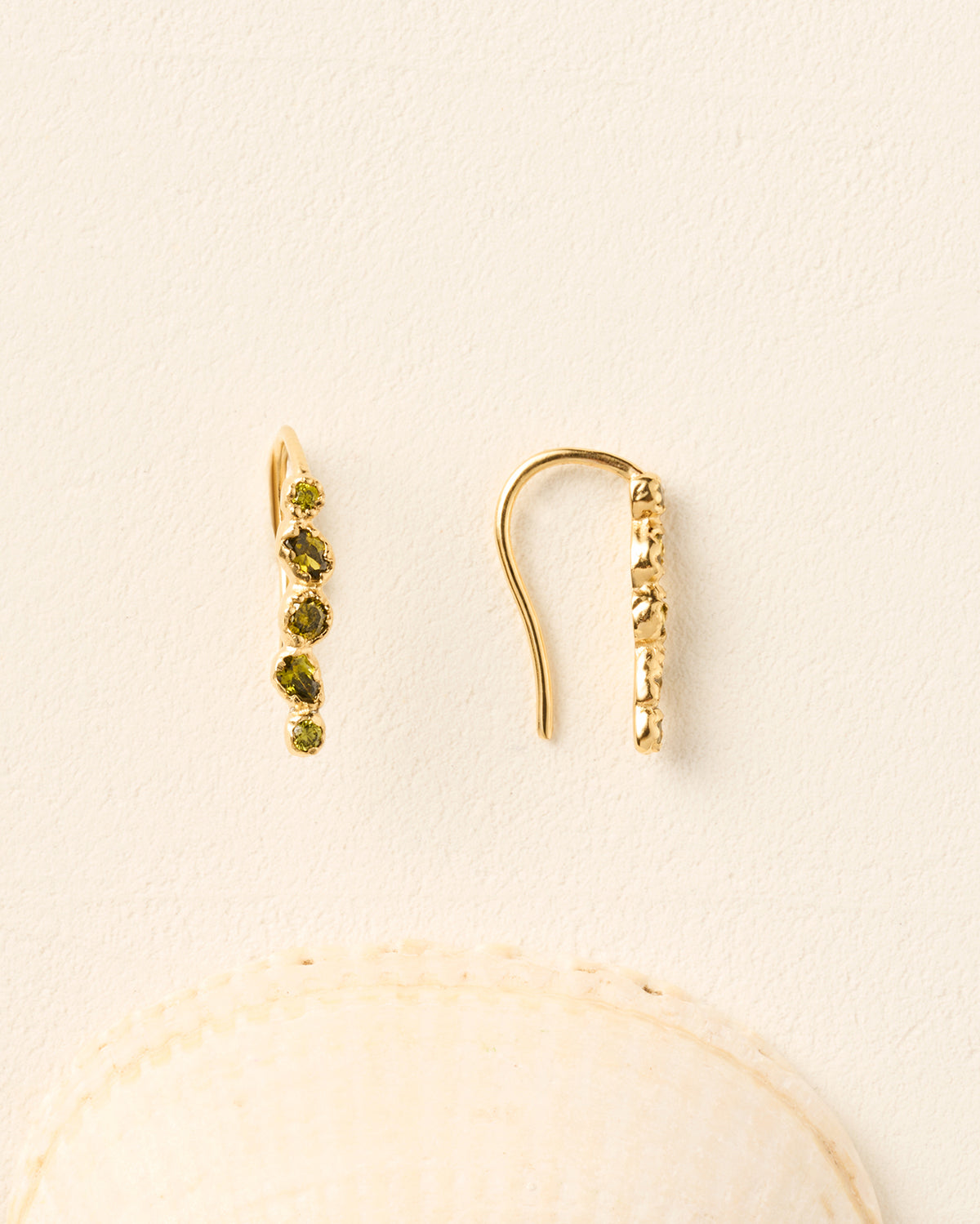 Gold drop earrings featuring five hand-set, deep green stones with organic, irregular settings on a textured cream background.