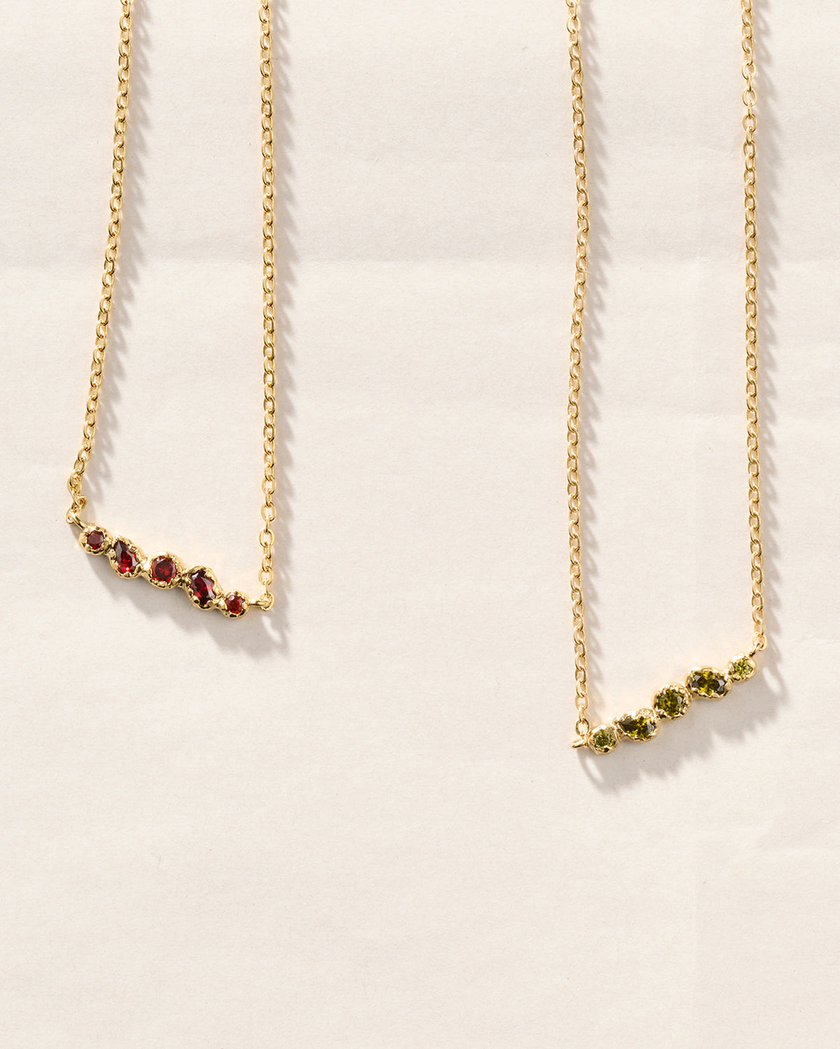 Collares de cadena dorados con colgantes orgánicos con cinco piedras rojo intenso y verdes engastadas a mano, sobre fondo texturizado.