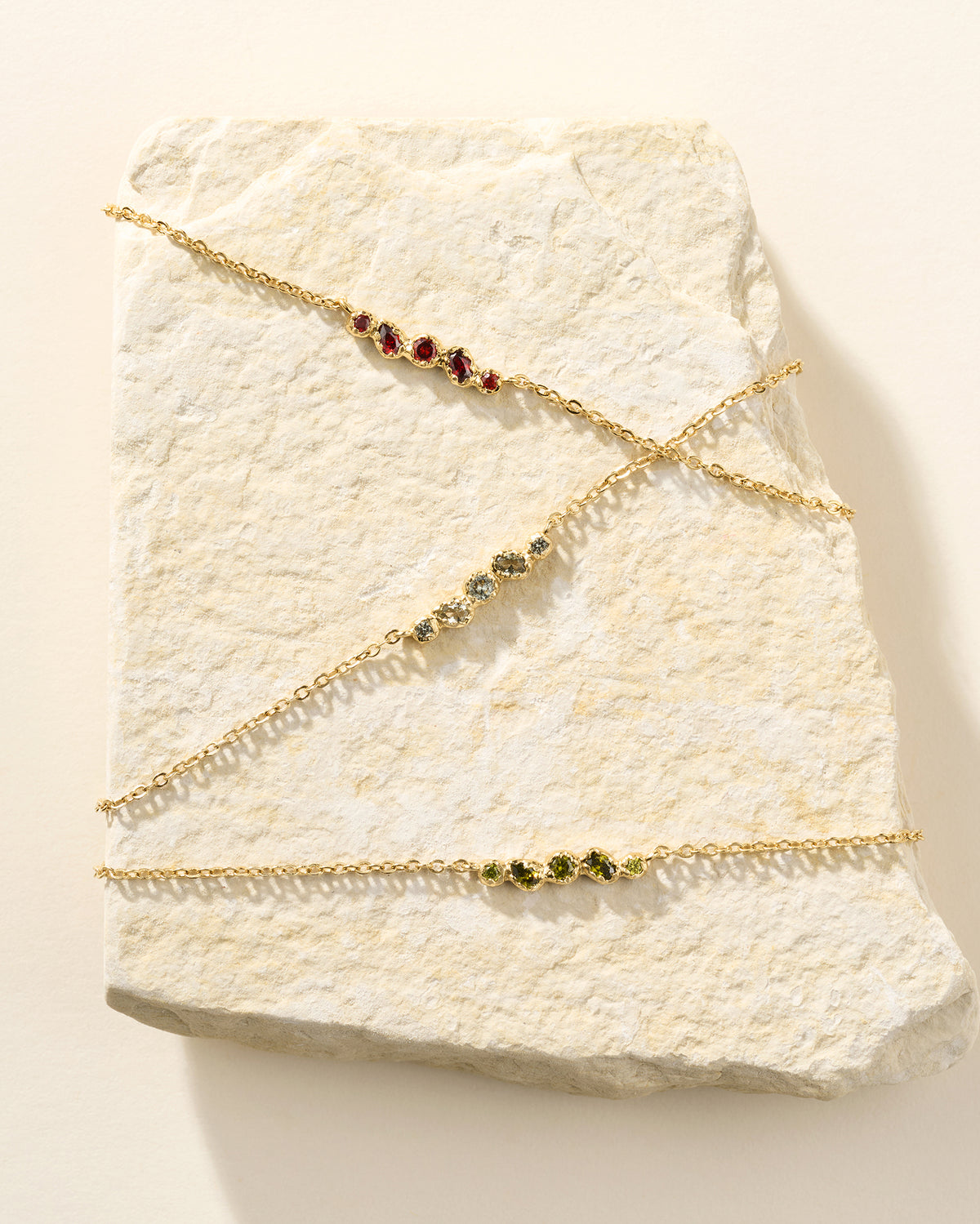 Tres delicados collares de cadena dorados con racimos de cinco pequeñas piedras de formas orgánicas en rojo, verde oliva y verde.