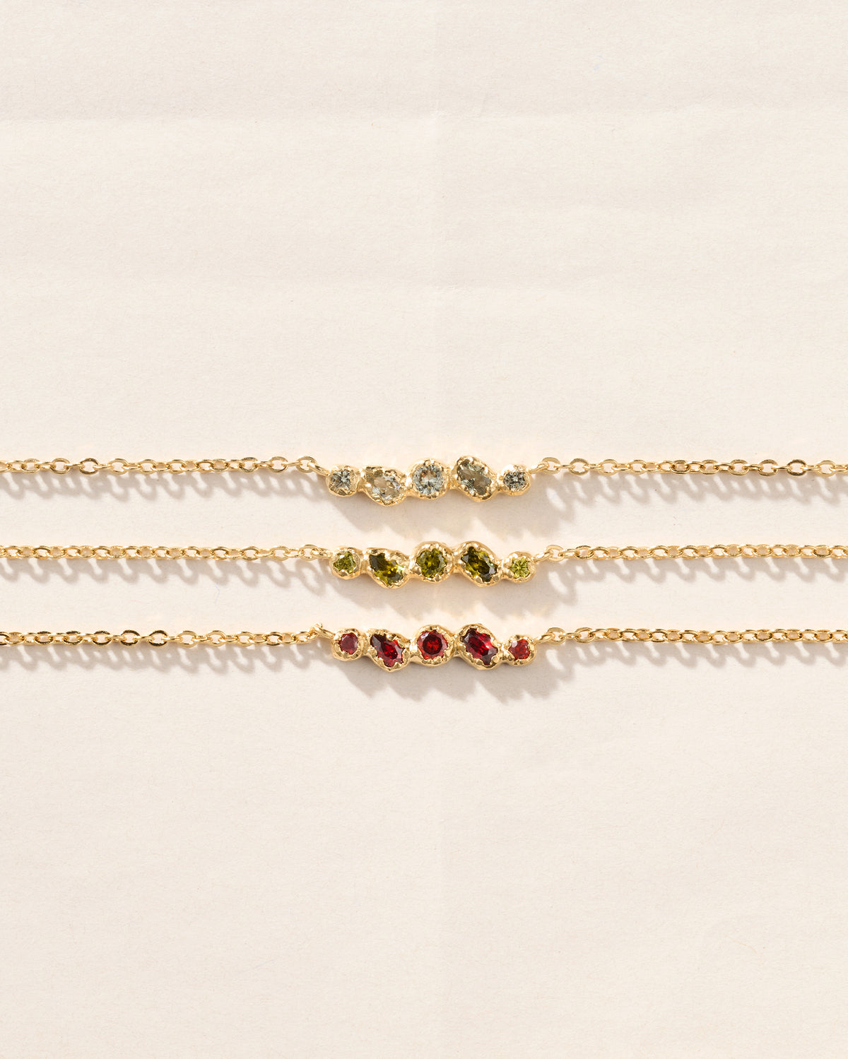 Tres collares dorados con colgantes orgánicos engastados con cinco piedras en azul verdoso, verde oliva y rojo.