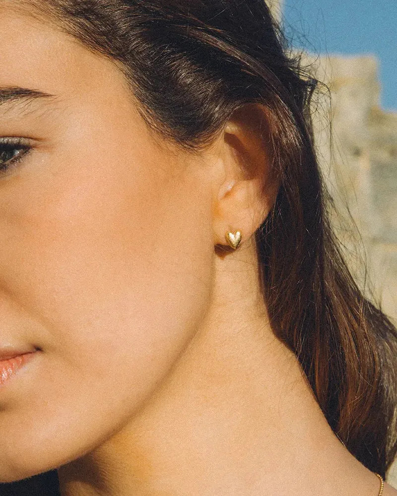 Corà gold heart stud earrings on a woman's earlobe.