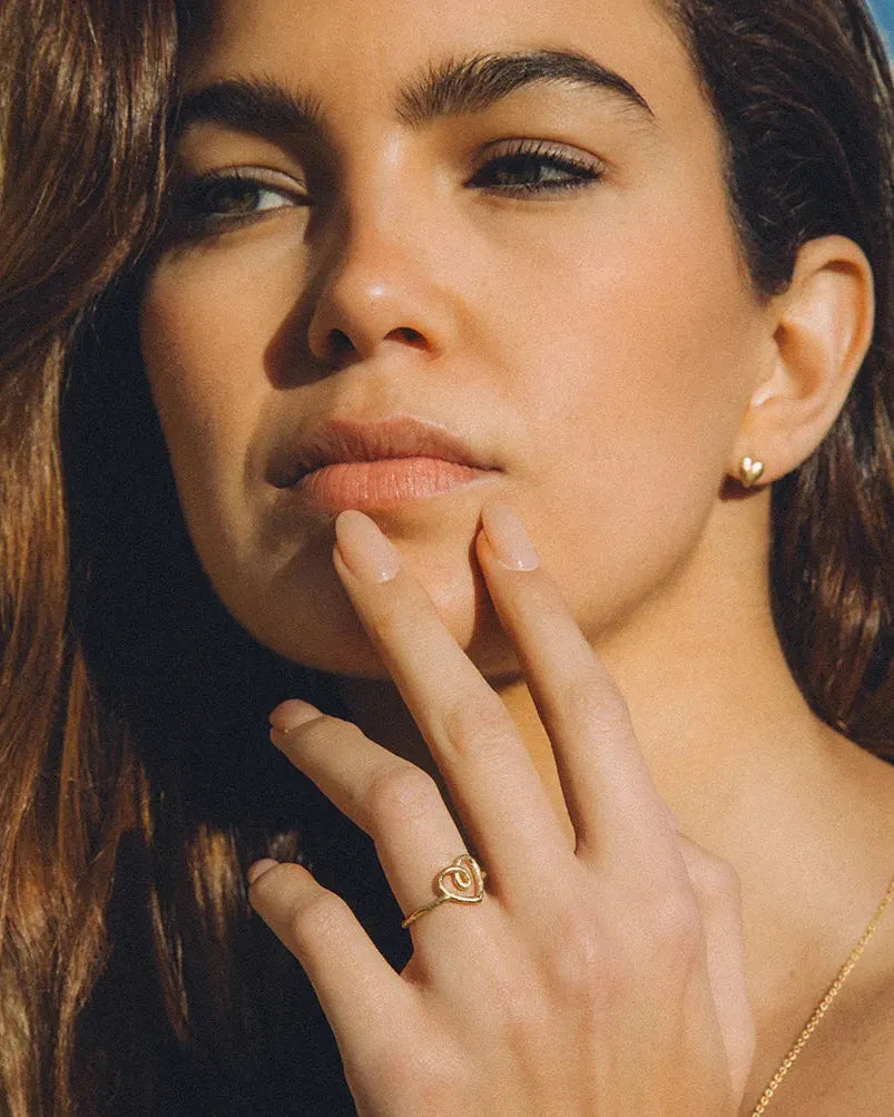 Woman wearing small gold heart stud earrings and a matching gold heart-shaped ring.