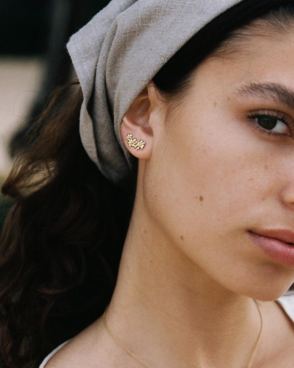 Gold Rosaria ear-climber with three delicate flowers on a woman's ear, minimalist style.
