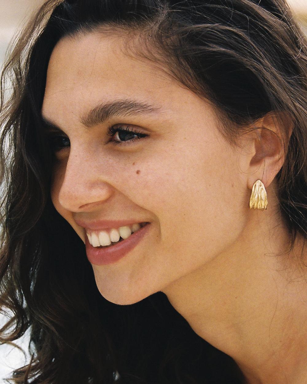Smiling woman wearing a single gold Lina earring with an organic, rippled design.