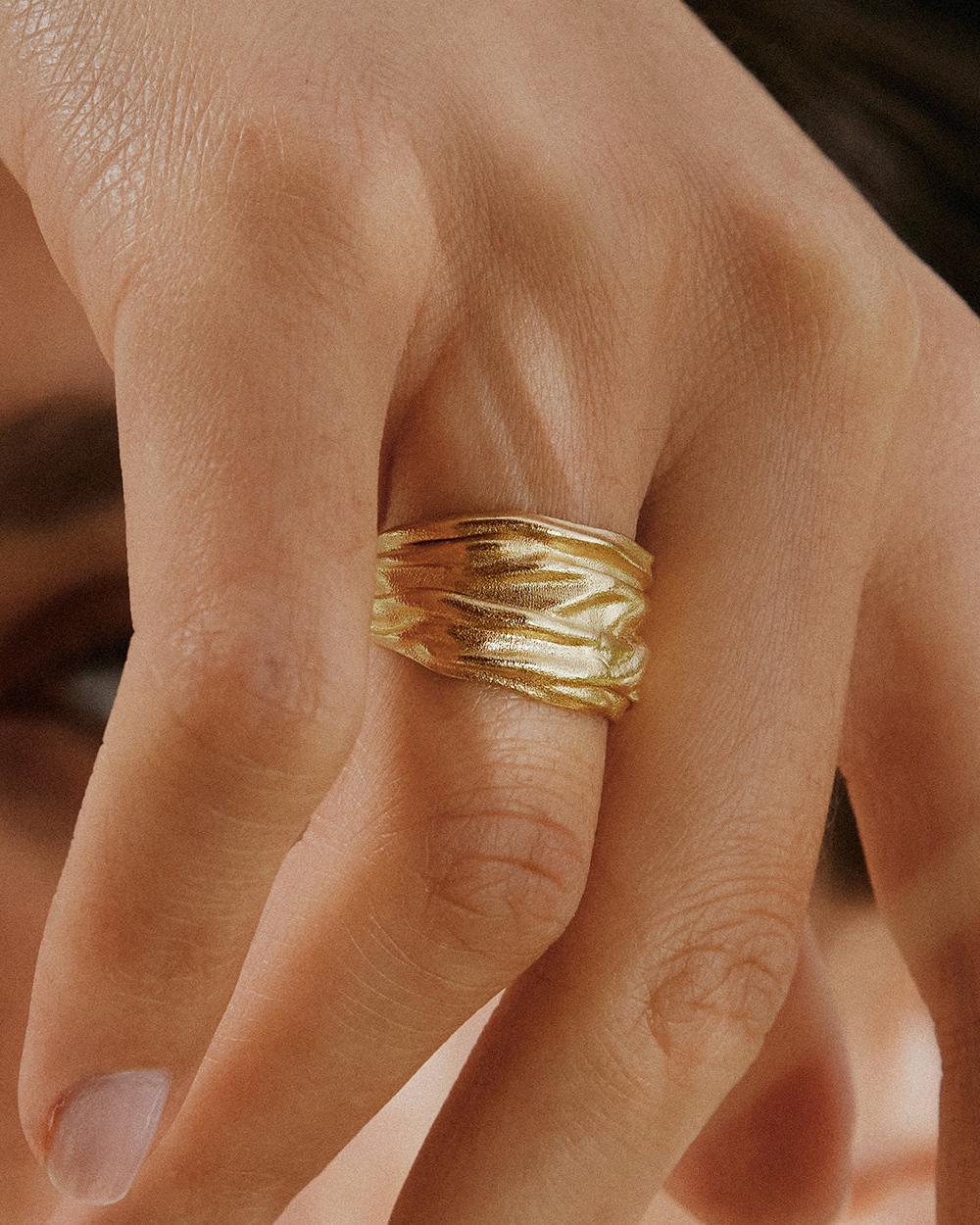 Anello Lina con una larga fascia dorata testurizzata dal design organico ondulato, indossato al dito.