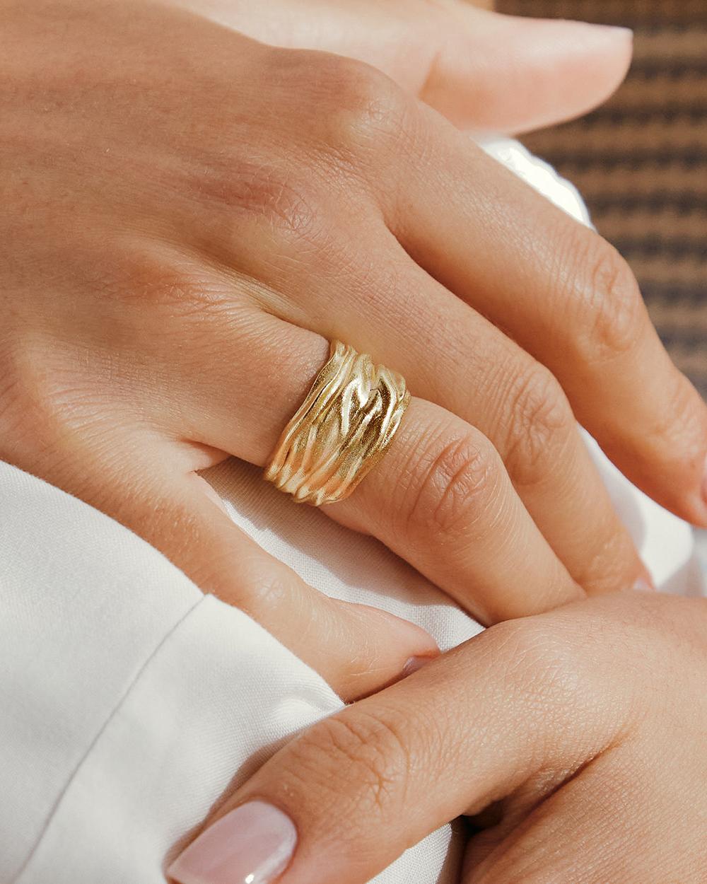 Anello Lina dorato con una larga fascia testurizzata dalle ondulazioni organiche simili a onde, indossato al dito.