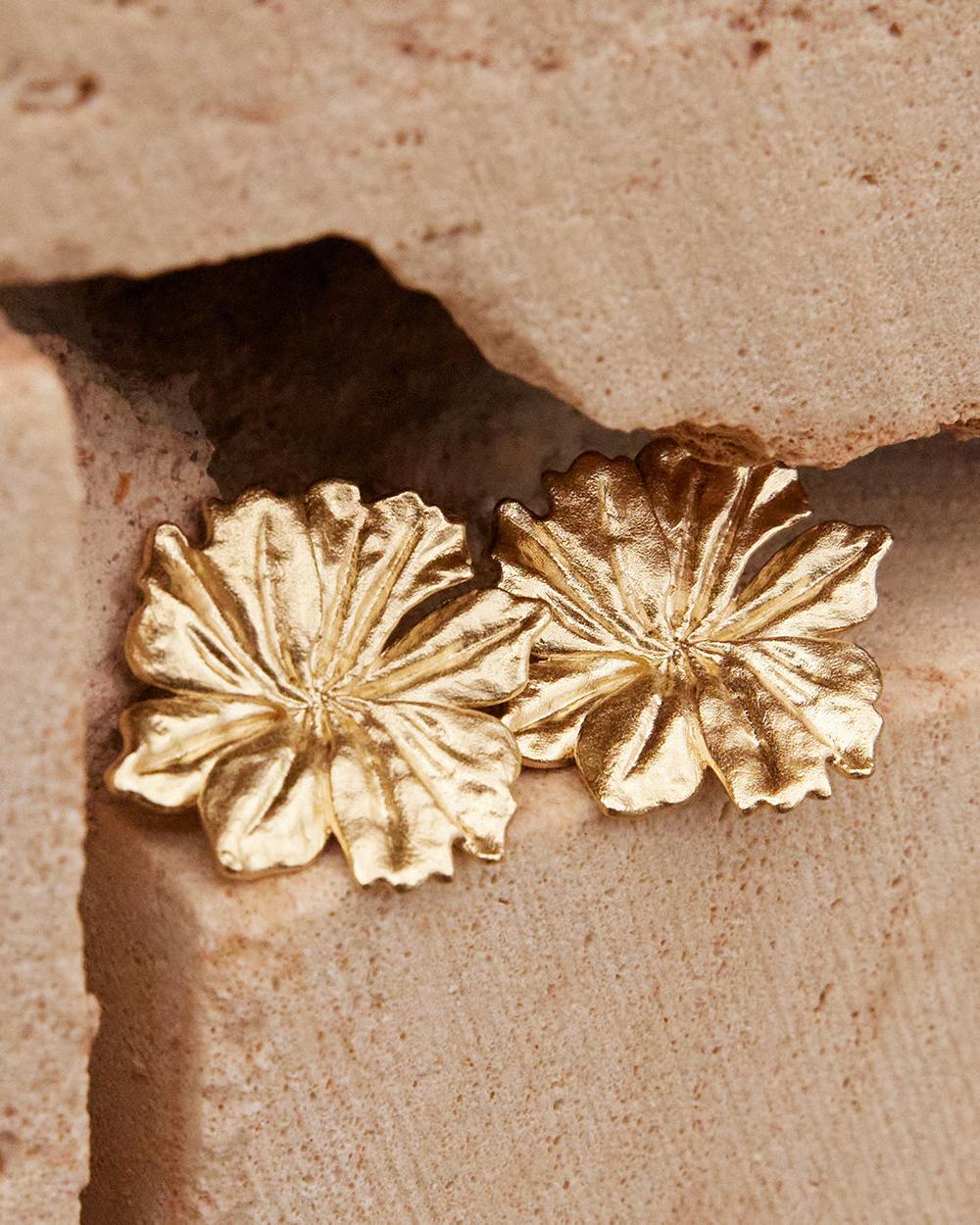 Pair of large, textured gold Adonis flower earrings resting on light brown stone.