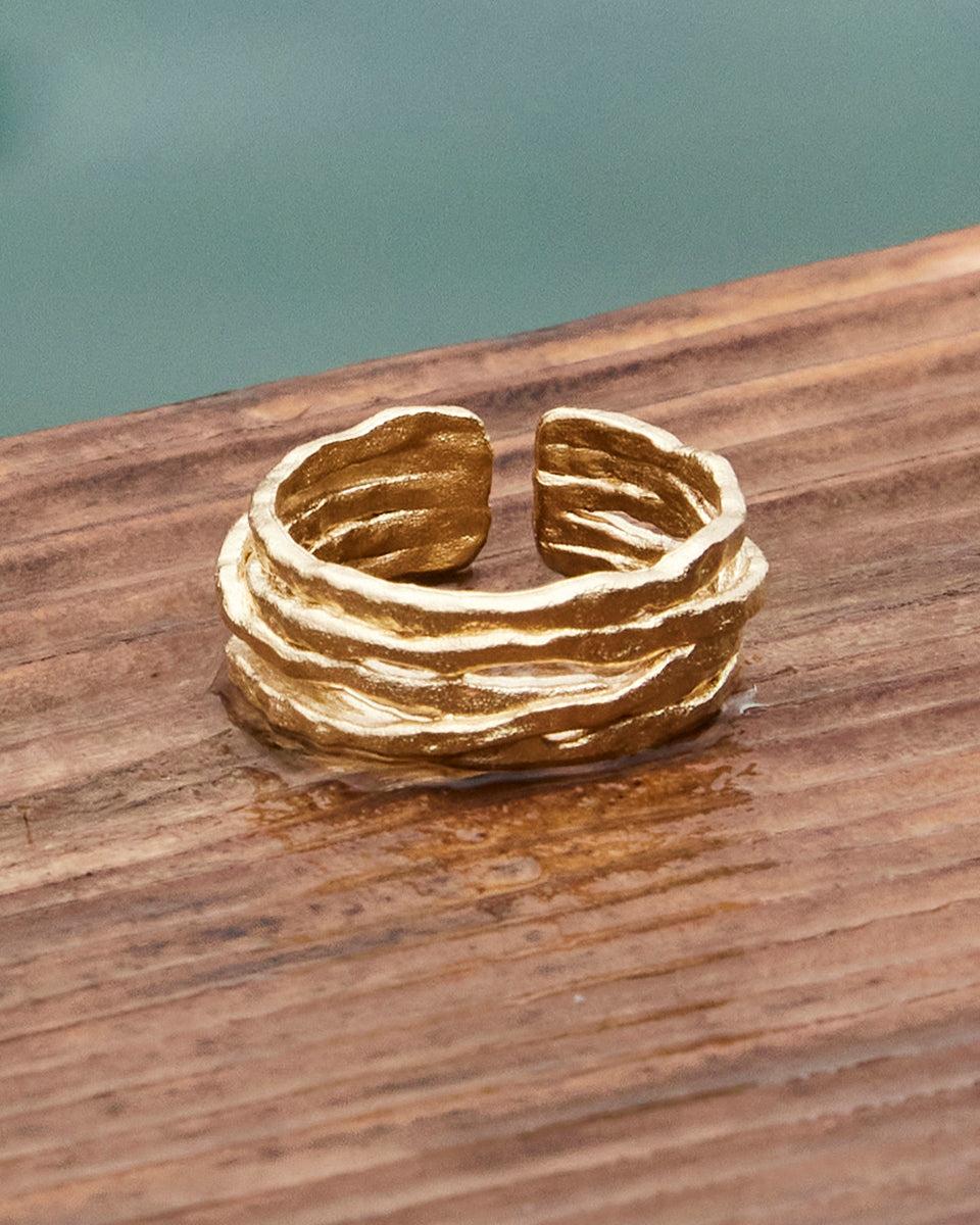 Gold coral ring with organic, textured lines on a wooden surface.