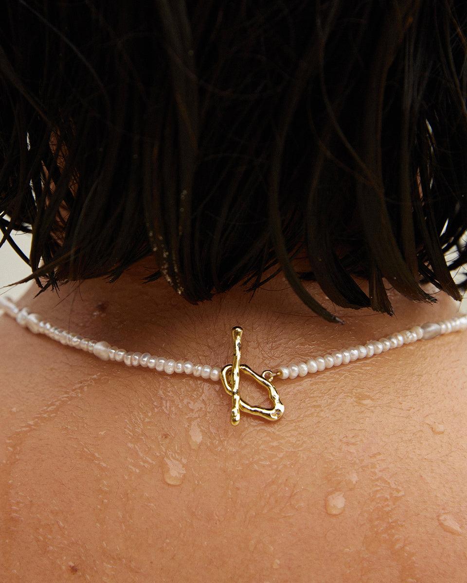 Oia Choker: White and grey freshwater pearl choker with a unique gold toggle clasp on a wet neck.