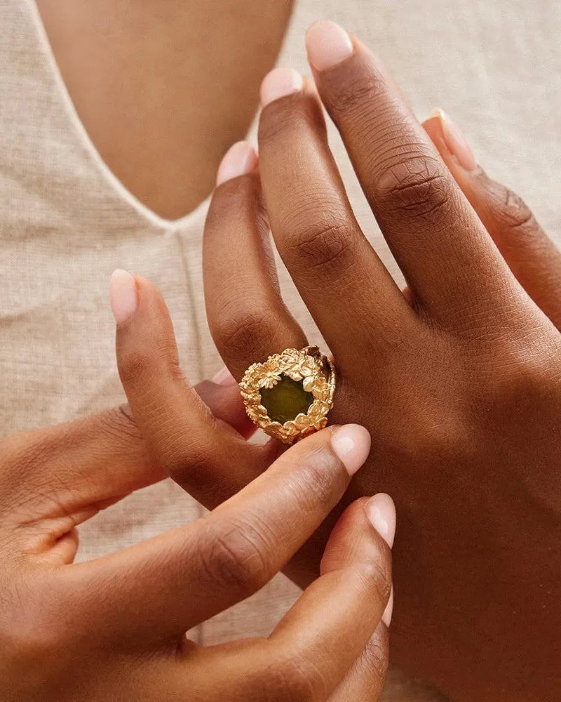 Gold Hespé chunky ring with a striking green stone cradled in a bed of flowers, worn on a hand.