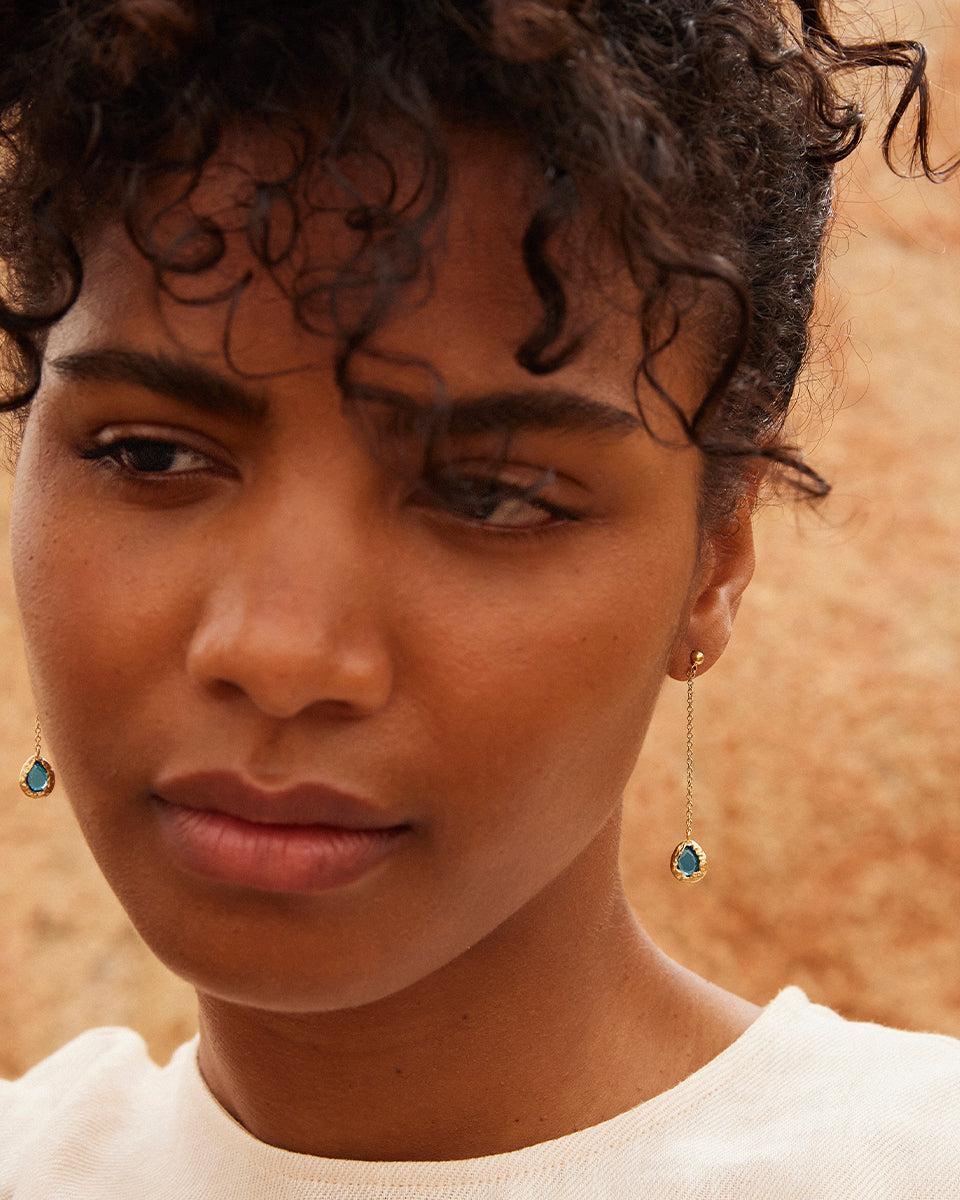 Lysia blue long earrings with drop-shaped pendants, blue stones, and textured gold.