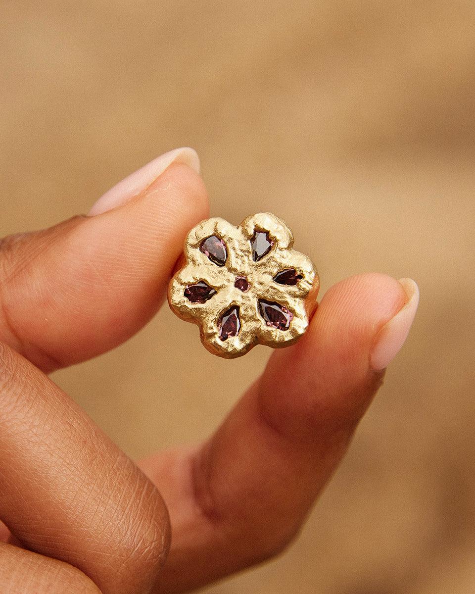 Gold Rita Ring with deep rosewood flower-shaped stone held between two fingers.