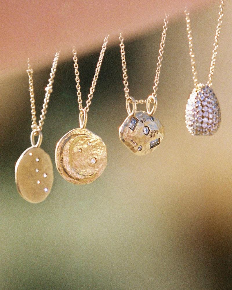 Rafael gold moon pendant necklace with inlaid white stones, alongside three other gold necklaces.