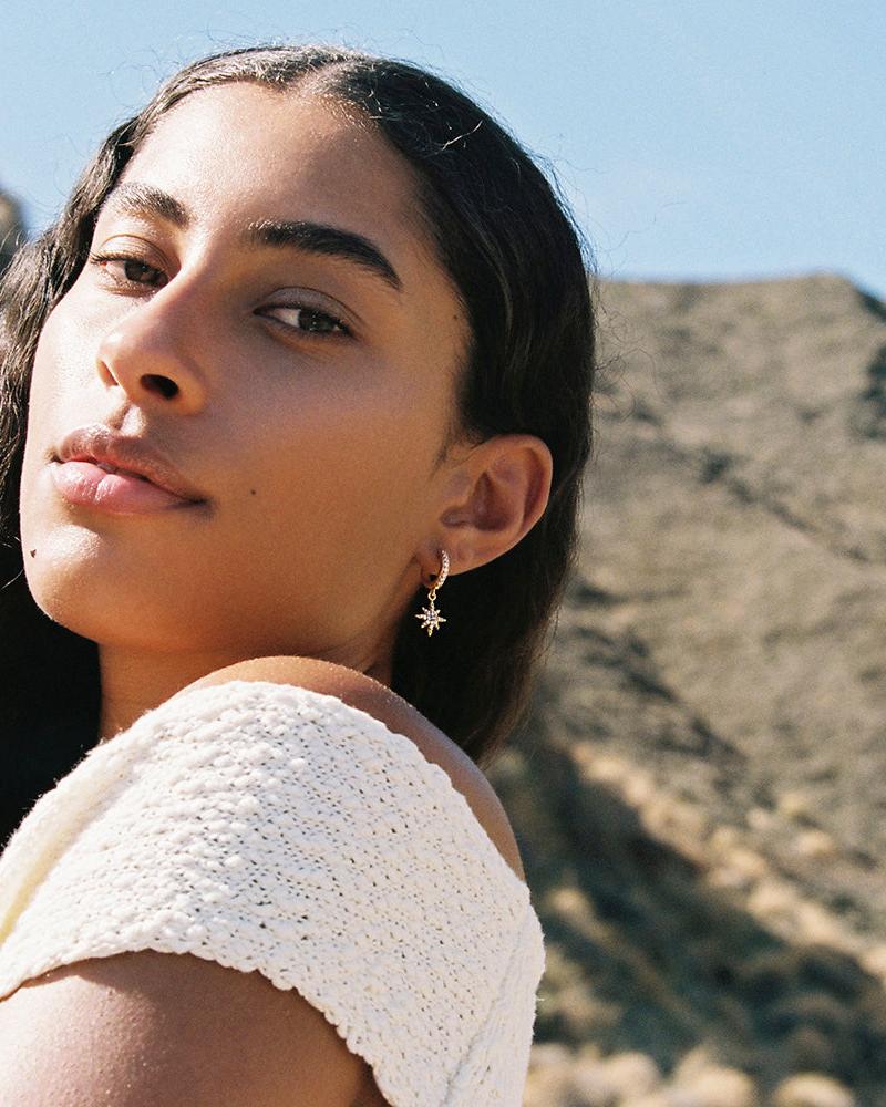 Gold hoop Celia earrings with a pavé-set white stone star pendant on a model.