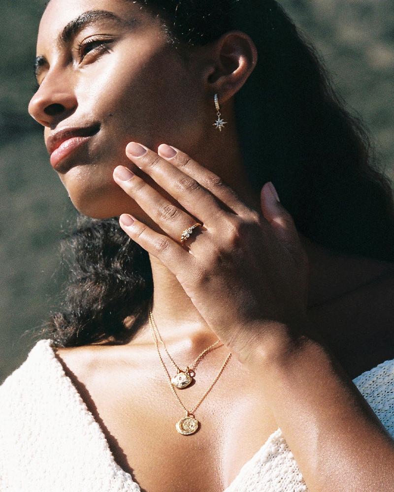 Woman wearing a gold Pépi nugget pendant necklace with white stones, matching ring, and starburst earring.