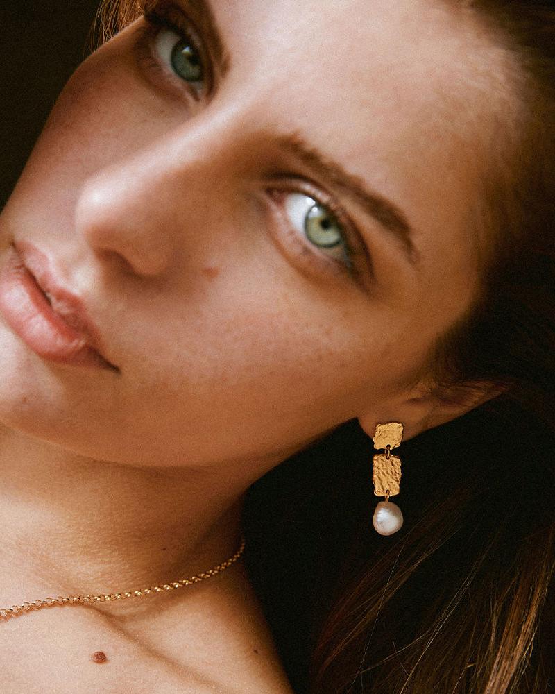 Gold Lythos drop earrings with textured rectangular panels and a pearl pendant.