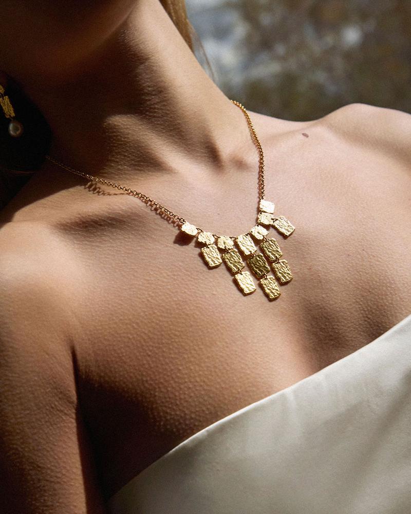 Gold Lythos necklace with textured, hammered rectangular panels in a layered, cascading design.