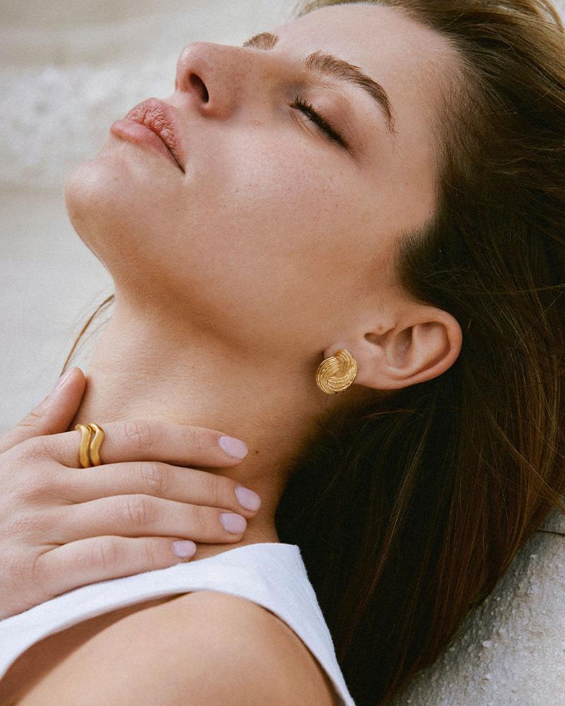 Gold Claudia chunky twist knot earrings with ridged, domed, wave-like design on a model.