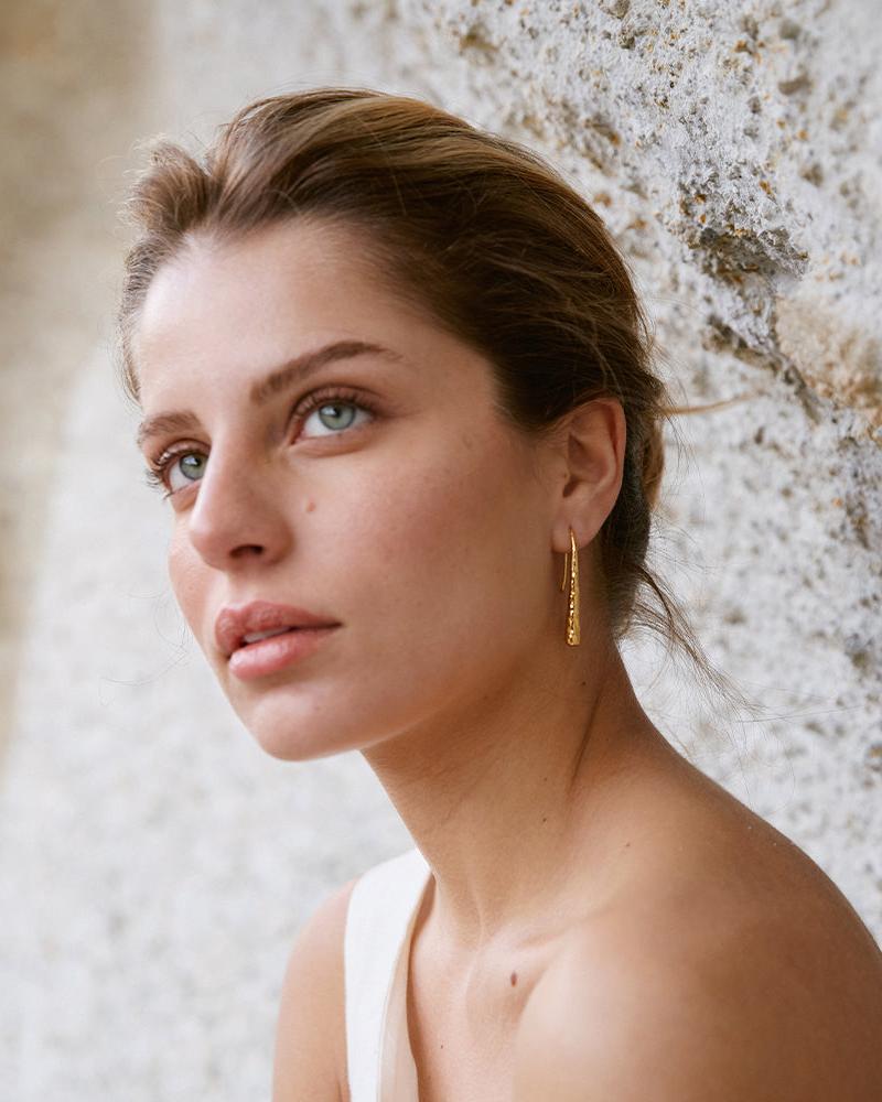 Thétis gold hammered drop earrings with a slim, molten design on a woman.