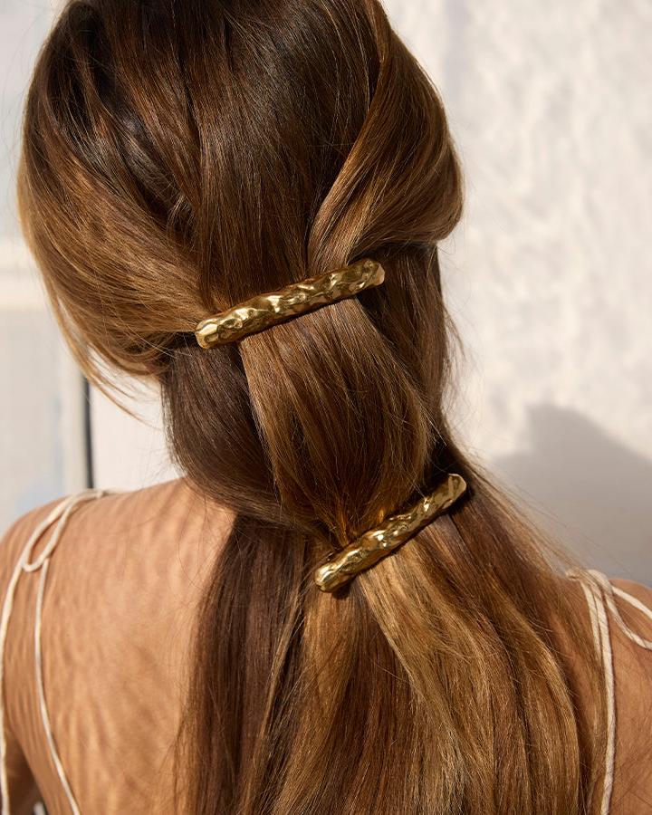 Two gold Nina hair clips with a hammered, organic texture styled in long brown hair.