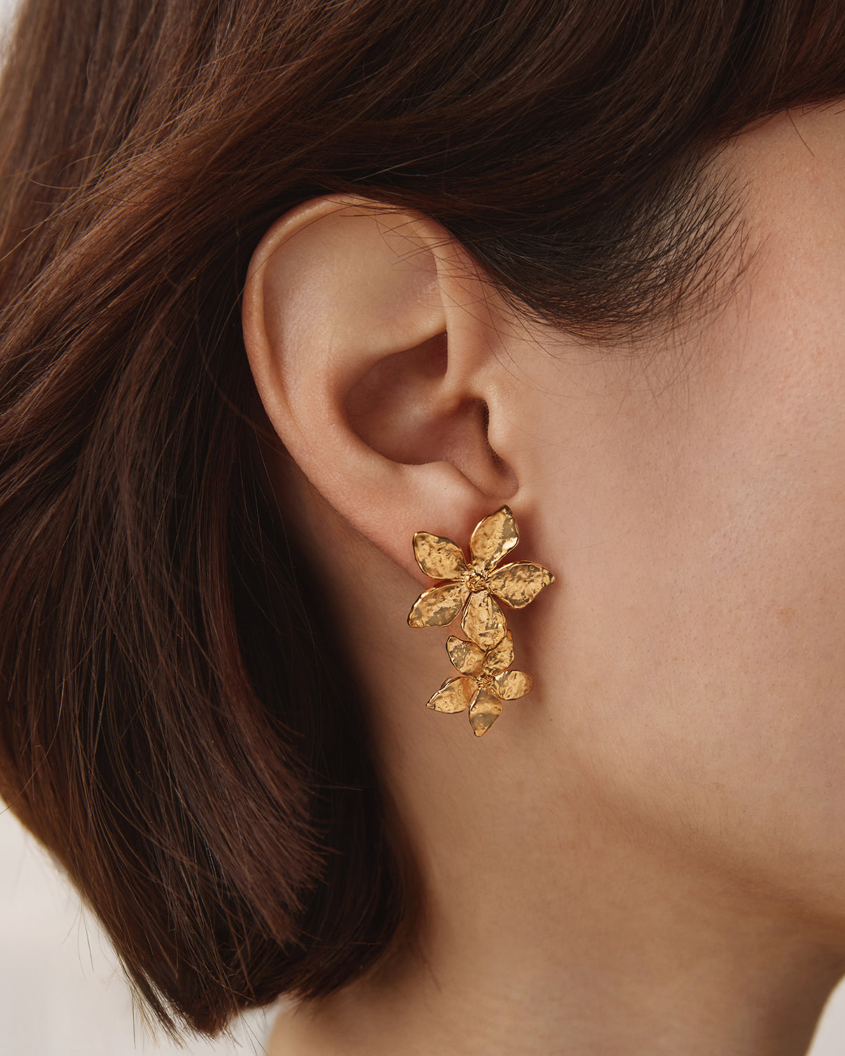 Gold-toned Thalla drop earrings featuring two hammered five-petal flower pendants worn on an earlobe.