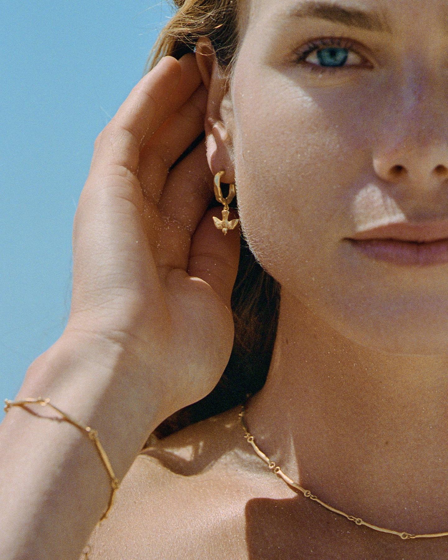 Gold mini-hoop earring featuring a small, detailed flying bird pendant with outstretched wings on a woman.