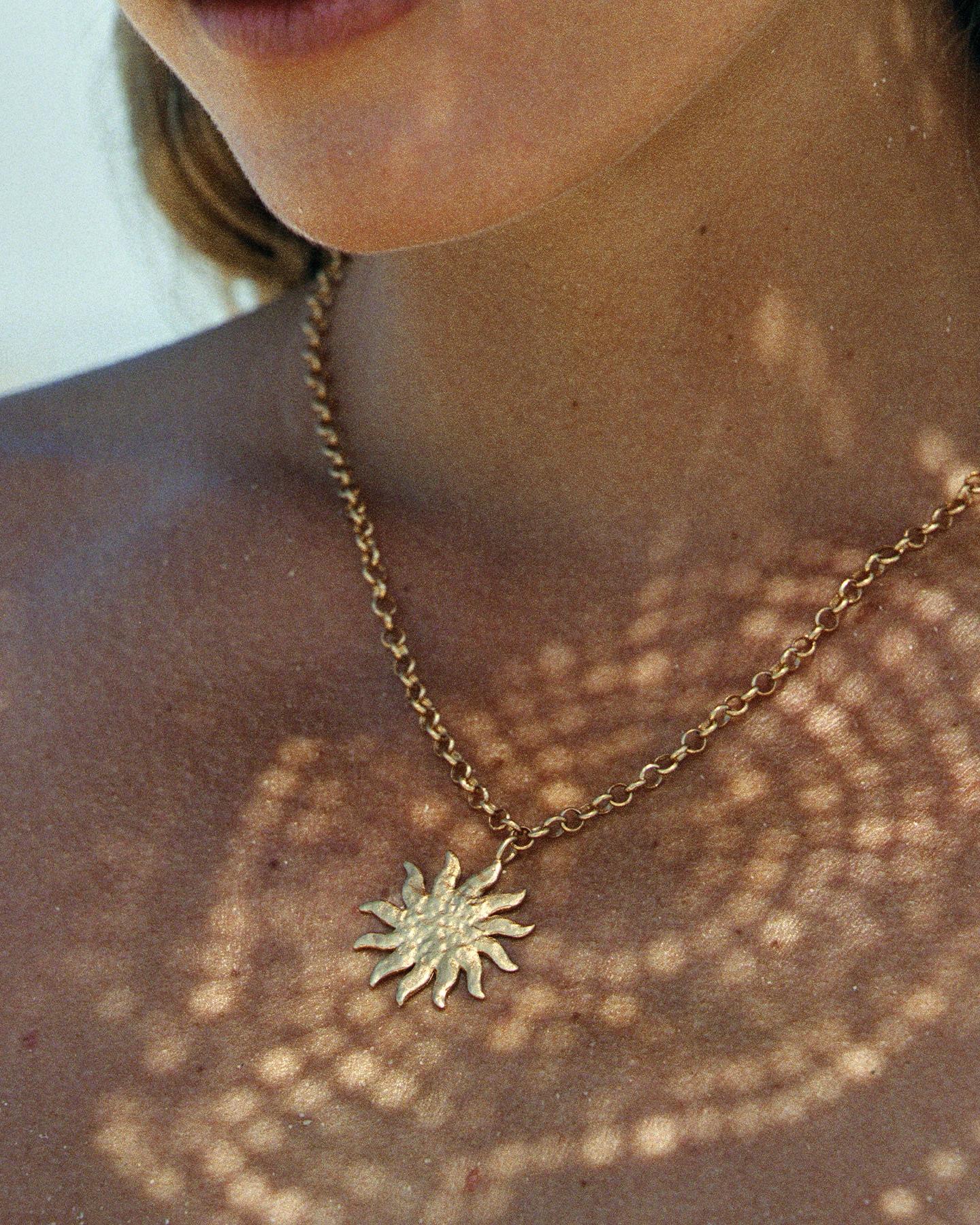 Gold Helio sun pendant necklace with hammered texture and wavy rays on a large rounded-link chain.