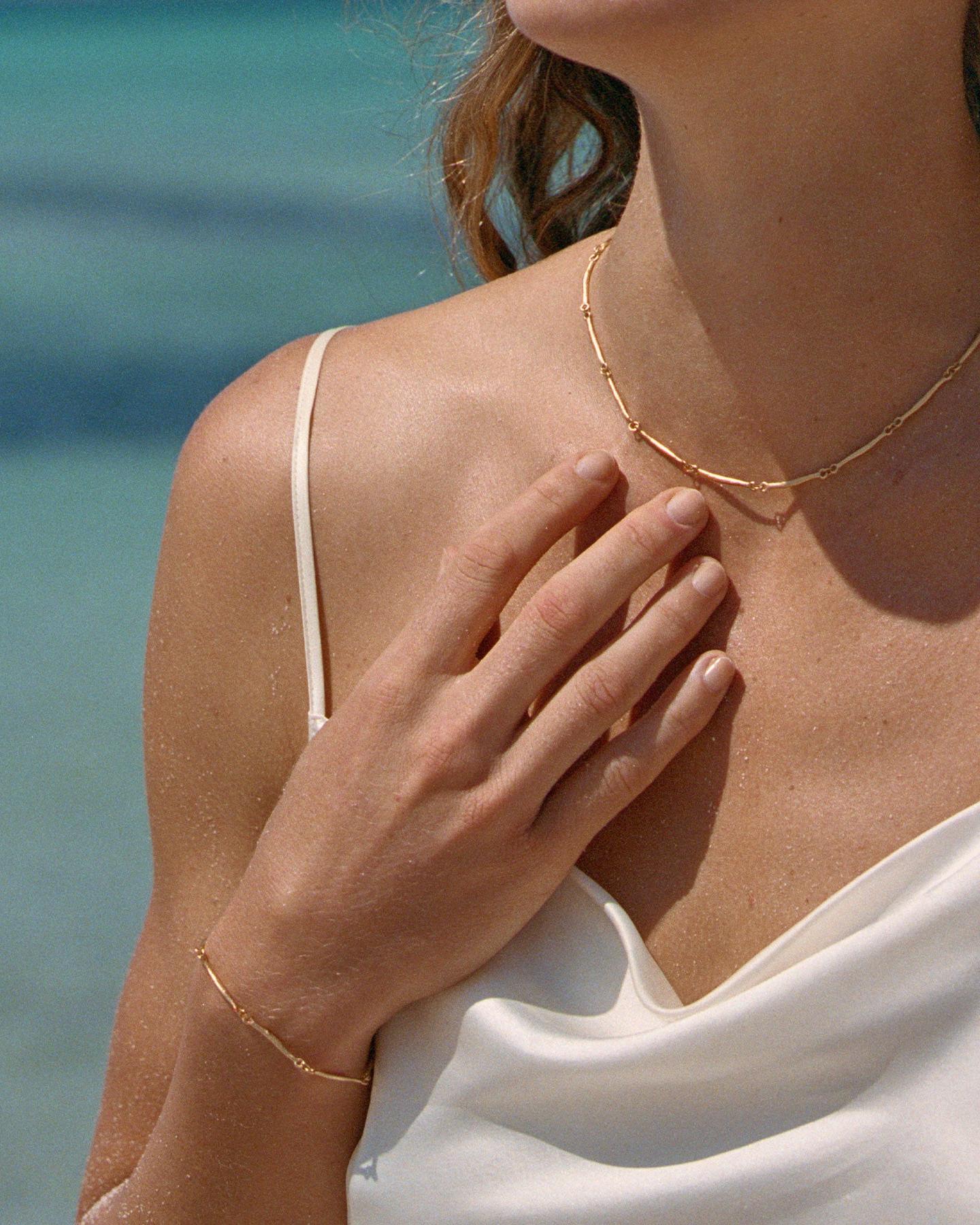 Gold Enea bracelet with hammered bar links on a woman's wrist, matching necklace visible.
