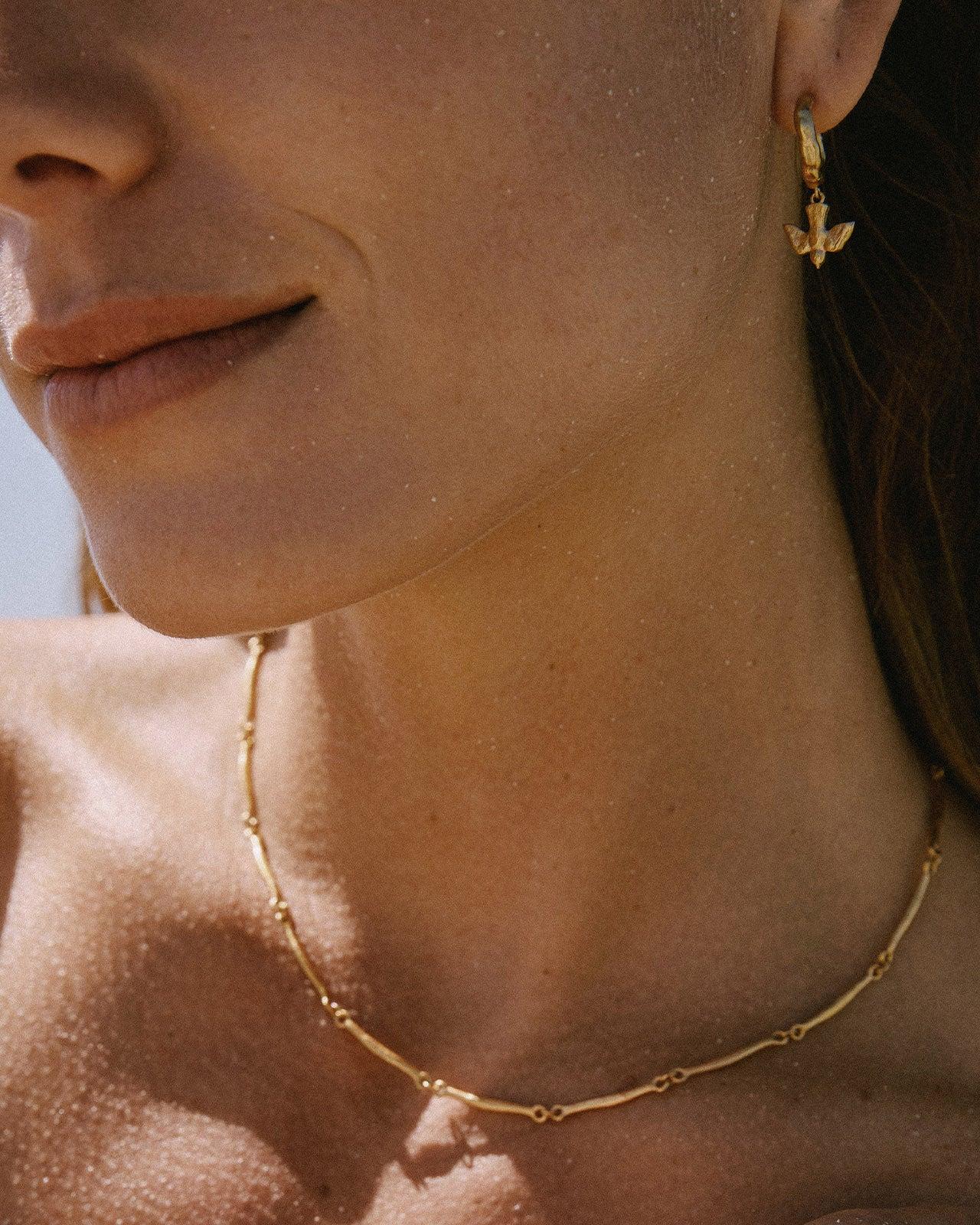 Gold mini-hoop earrings featuring a detailed flying bird pendant with outstretched wings worn on a woman's ear.