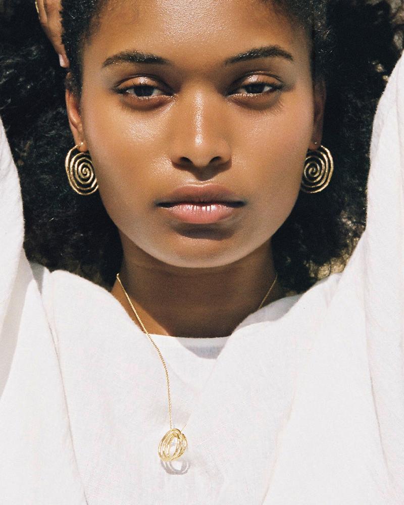 Woman wearing Nacci gold spiral earrings and matching pendant necklace.