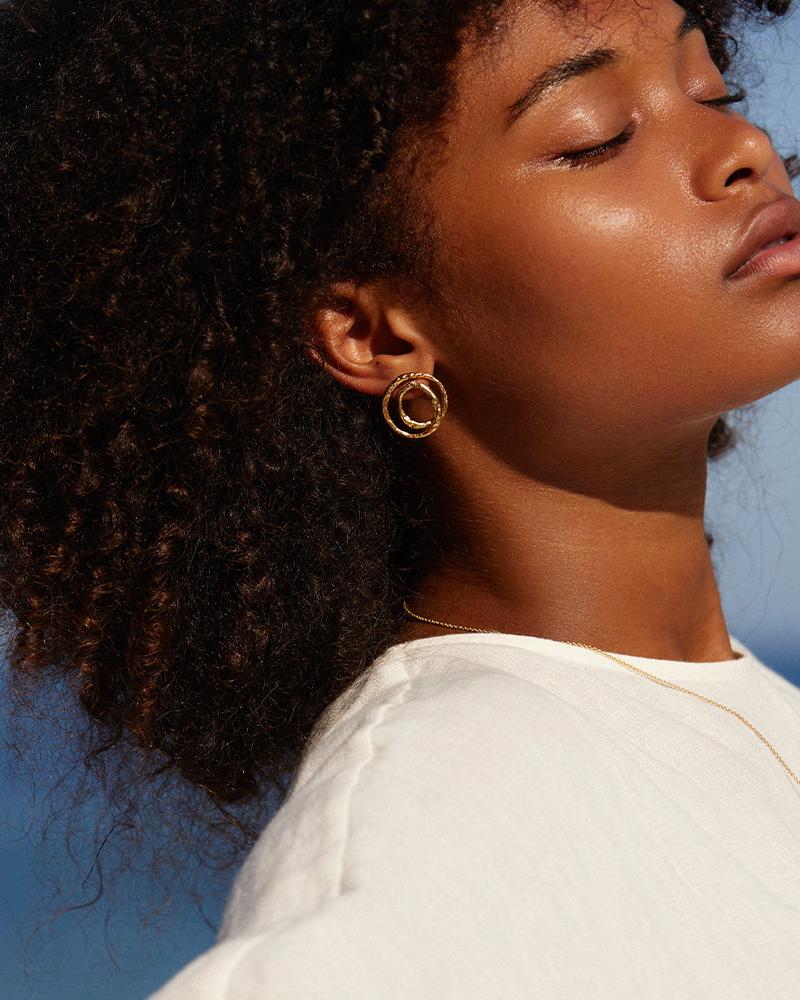 Gold Orecchi crossover earrings with twisted bands on a woman's ear.