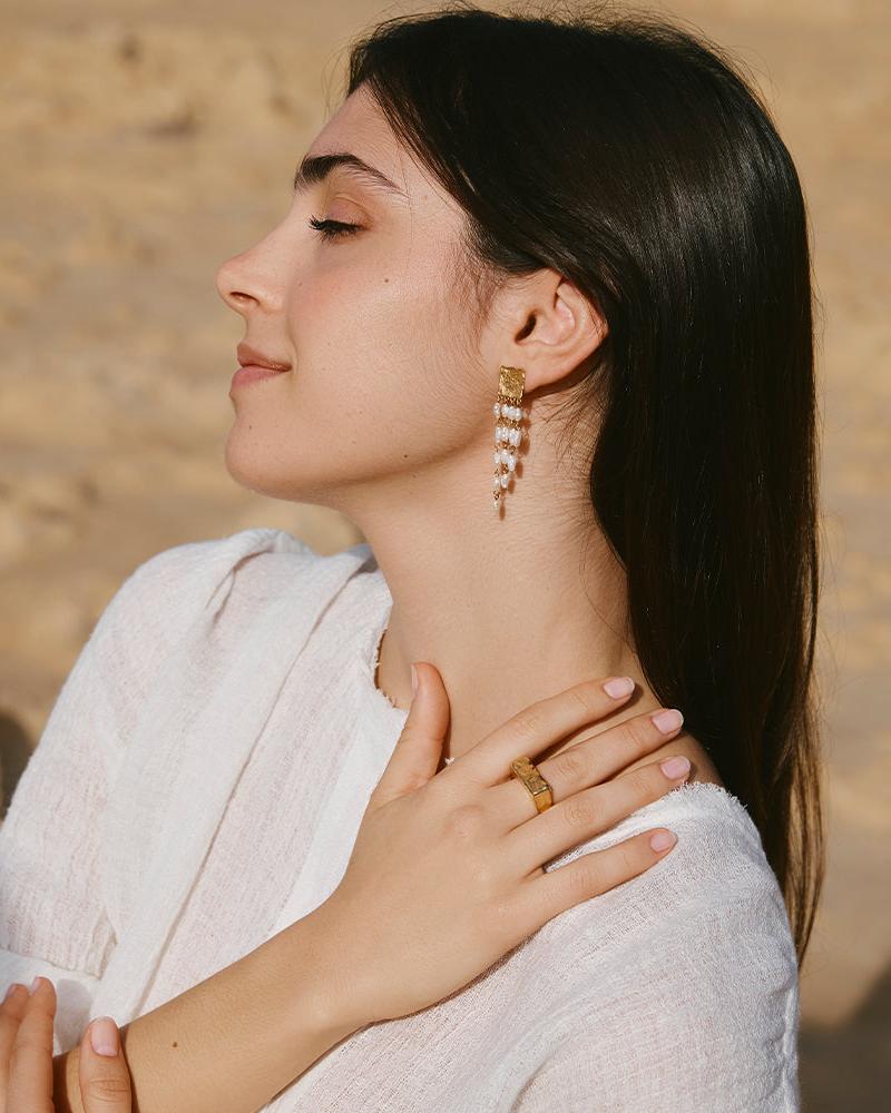 Woman wearing a chunky, hammered gold Octavia rectangle signet ring and matching earrings.