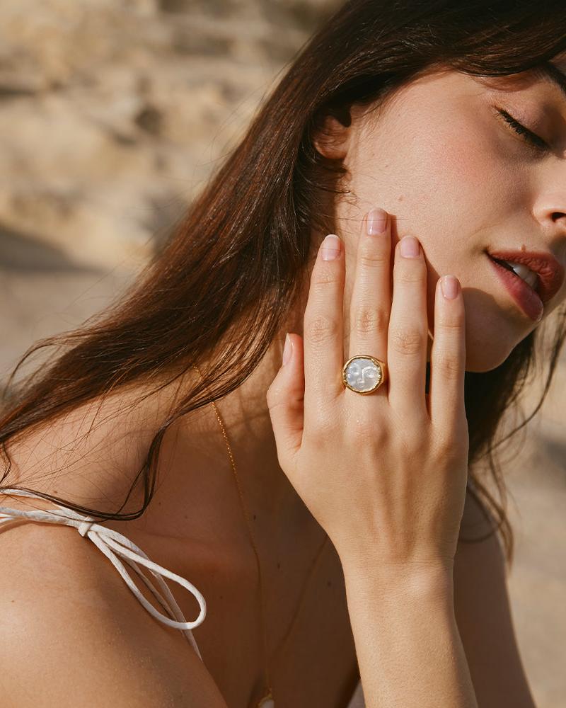 Hëna Ring: Luminescent mother-of-pearl moonface ring in a golden setting on a woman's hand.