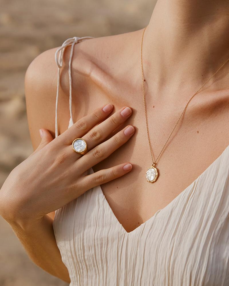 Hëna Ring: Luminescent mother-of-pearl moonface statement ring in a golden setting, worn on a hand.