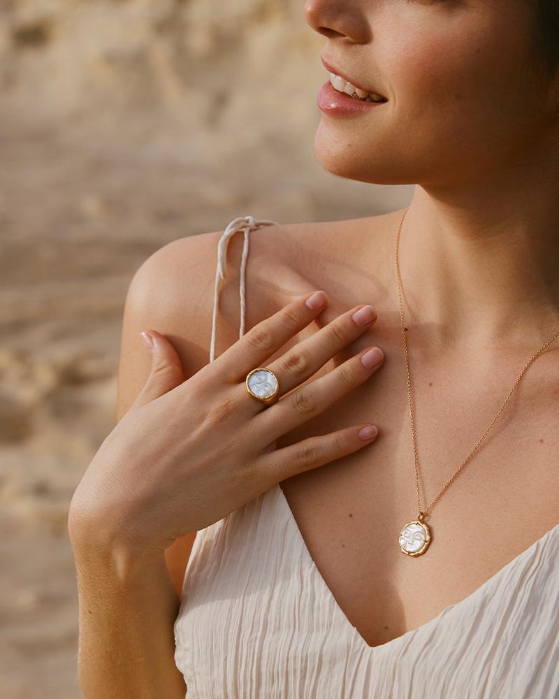 Woman wearing a Hëna necklace with a luminescent mother-of-pearl moonface pendant in a golden setting.