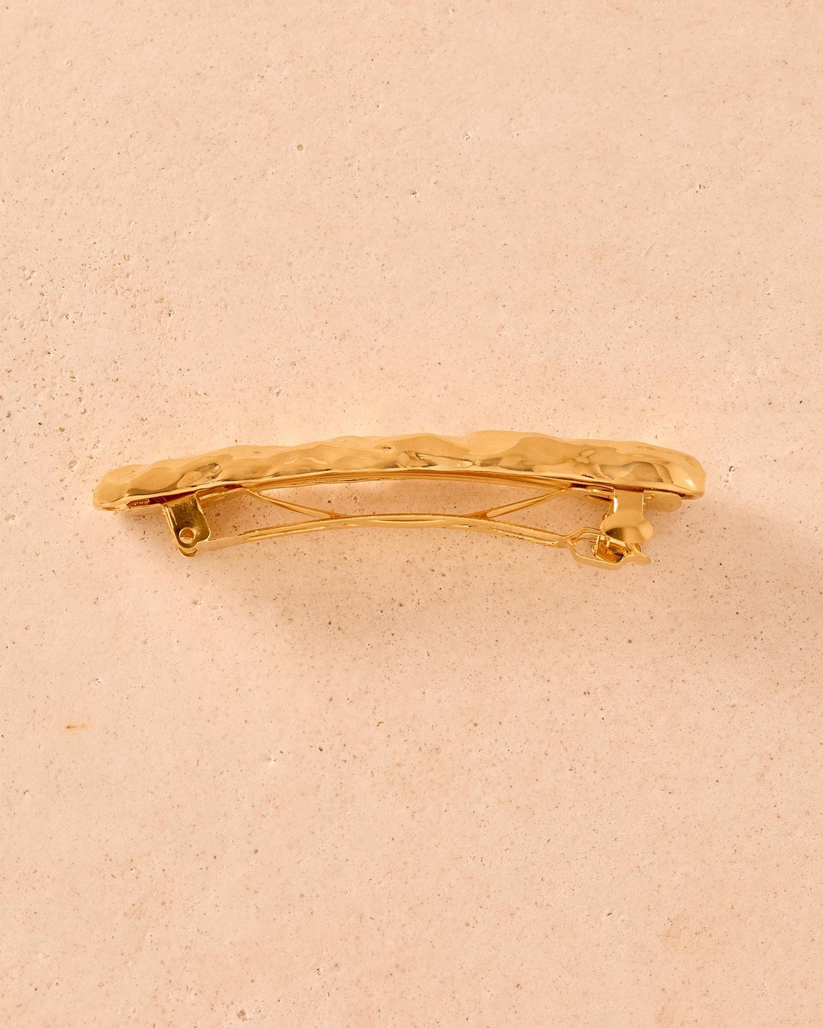 Goldfarbene Nina-Haarspange mit strukturiertem, gehämmertem Metallfinish vor neutralem Steinhintergrund.