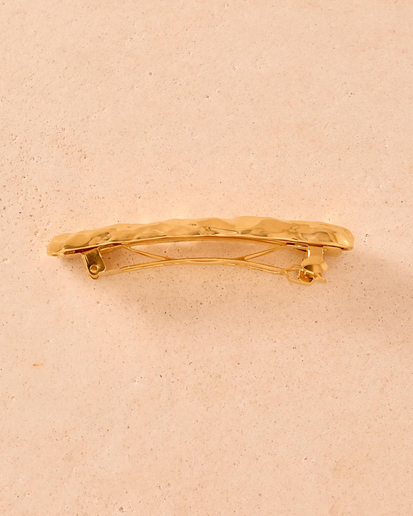 Gold Nina hair barrette with a textured, hammered metal finish on a neutral stone background.