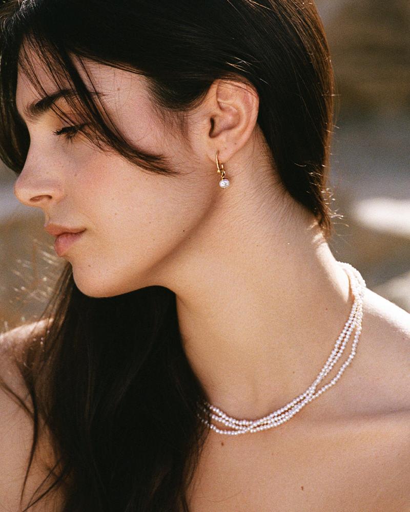 Gold twisted hoop Phaedra earrings with a dangling freshwater pearl, worn by a woman.