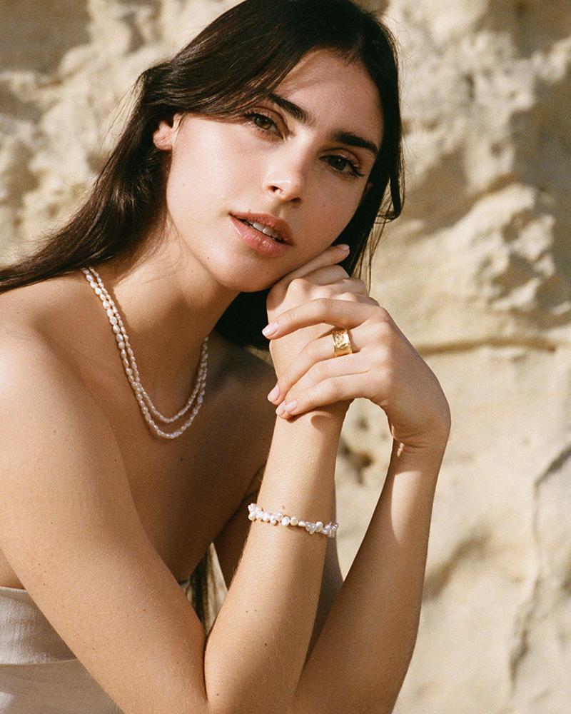 Woman wearing a dainty Estée bracelet with irregular white pearls and a gold ring.