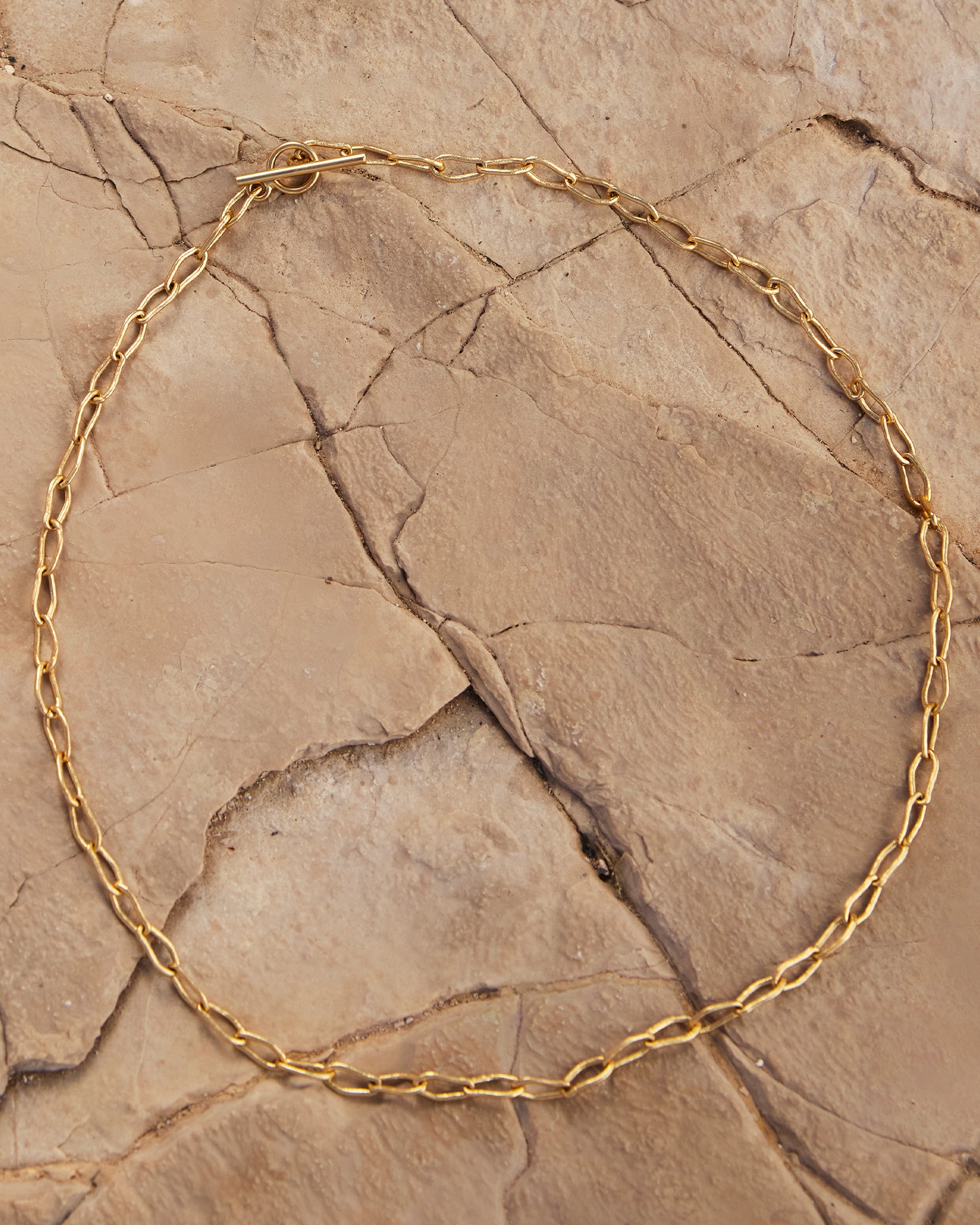 Gold Horace Mini Choker with intertwined links and sleek toggle clasp on a textured rock surface.
