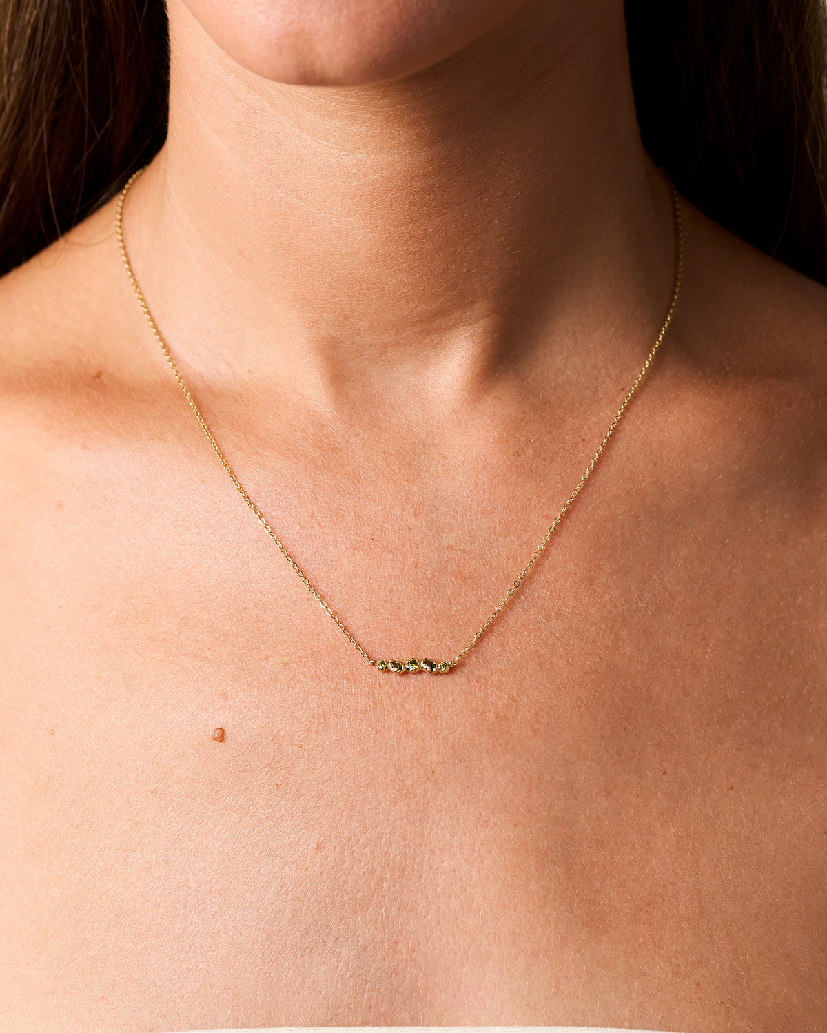 Collar de cadena dorado con cinco pequeñas piedras verde intenso de formas orgánicas, en el cuello.