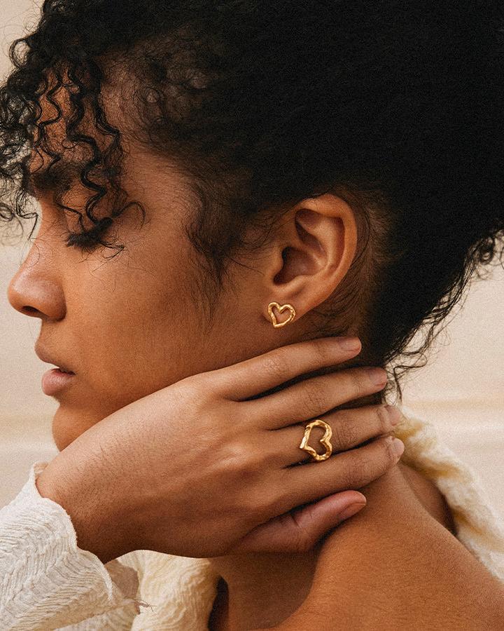 Gold Liora open-heart earrings and matching ring on a model's earlobe and finger.